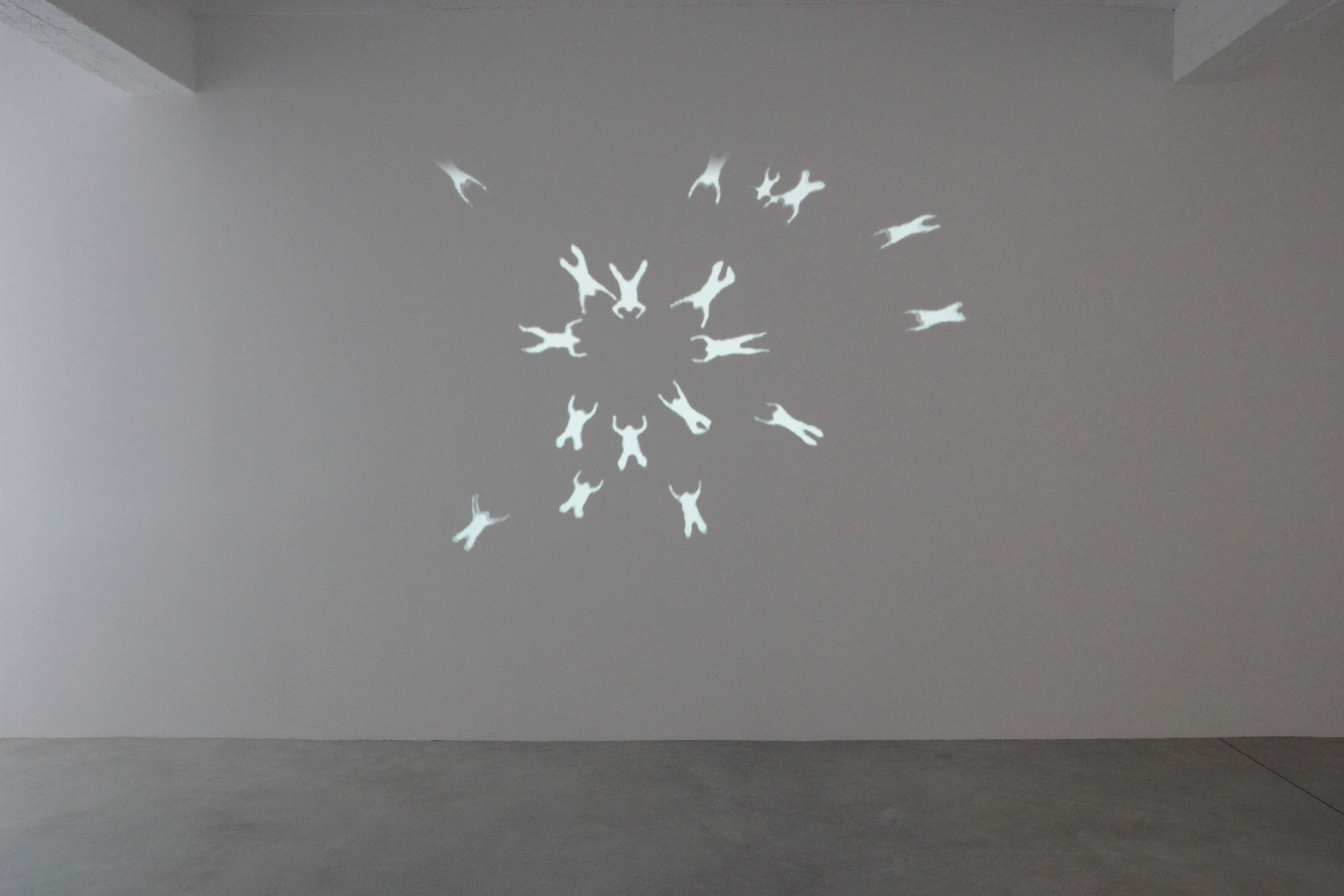 Fotografia projekcji pracy autorstwa Dominika Lejmana "Katedra 60s". Kadr na białą ścianę, na której wyświetlana jest projekcja humanoidalnych postaci.