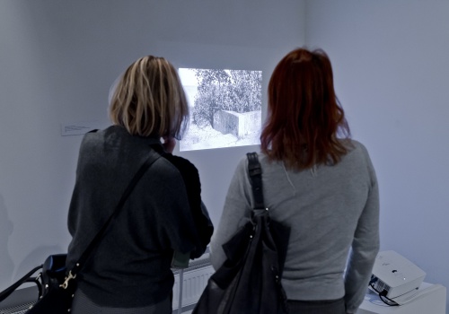 Zdjęcie, dwie uczestniczki wernisażu oglądają zdjęcia artystki wyświetlane na ścianie przez projektor.