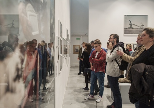 Zdjęcie, licznie zebrani uczestnicy wernisażu oglądają prace Michała Szlagi w przestrzeni Sali Wystawienniczej. Niektórzy uczestnicy robią zdjęcia telefonem.