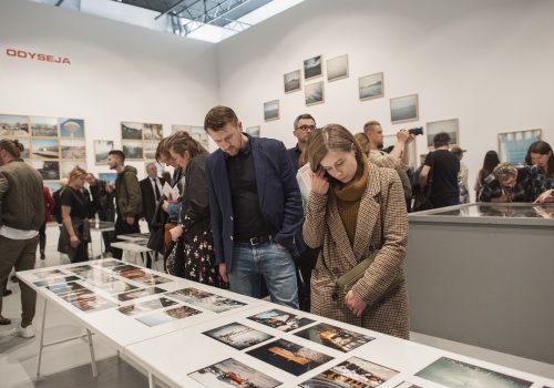 Zdjęcie, licznie zebrani uczestnicy wernisażu oglądają prace Michała Szlagi w przestrzeni Sali Wystawienniczej. Na pierwszym planie znajduje się szklana gablota, a przy niej dwójka uczestników.