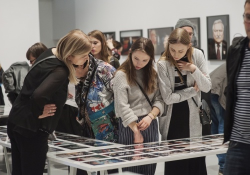 Zdjęcie, licznie zebrani uczestnicy wernisażu oglądają prace Michała Szlagi w przestrzeni Sali Wystawienniczej. Na pierwszym planie znajduje się szklana gablota, a przy niej kilkoro uczestników.