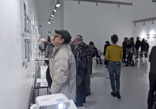 Zdjęcie, wnętrze Sali wystawienniczej podczas trwania wernisażu. Licznie zebrani uczestnicy oglądają prace artysty prezentowane na ścianach oraz w szklanych gablotach.