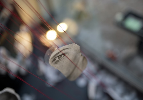Kadr na fragment instalacji artystycznej w postaci wyciętego fragmentu fotografii twarzy, zawieszonego na czerwonych sznurkach w galerii LKW.
