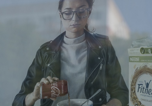 2.	Zbliżenie na obraz przedstawiający postać młodej kobiety nalewające Coca-Cole do miski. Obok stoi pudełko z płatkami śniadaniowymi oraz przewrócony karton z mlekiem.