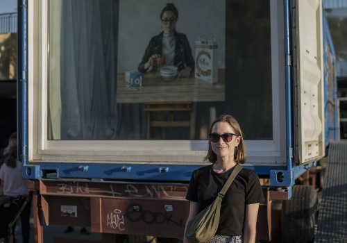 10.	Uśmiechnięta młoda kobieta stojąca przed oknem galerii LKW, za którym wyeksponowano obraz.