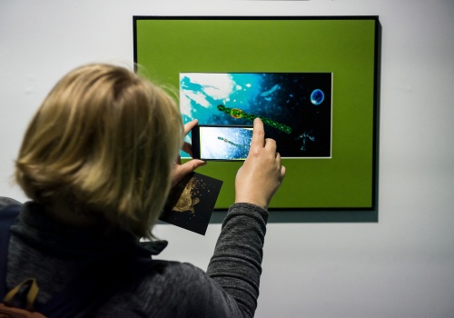2.	Kadr na postać wykonującą smartfonem fotografię jednej z prac prezentowanych na wystawie. 