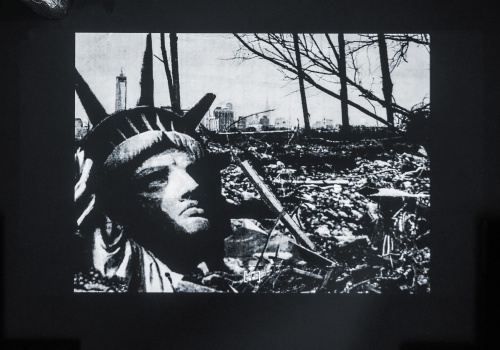 Kadr z czarno – białego filmu. Ruiny miasta, wraz ze zniszczonym, górnym fragmentem Statuy Wolności.