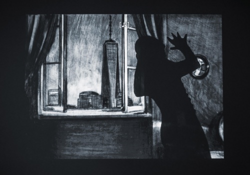 Czarno – biały rysunek przedstawiający nocną scenerię miasta z perspektywy okna, węwnątrz mieszkania, w którym widoczny jest kontur postaci wygiętej w geście przerażenia.