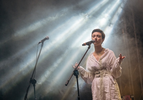 Kadr na wokalistkę zespołu VVelur, śpiewającą na zamglonej scenie Teatru Leśnego.