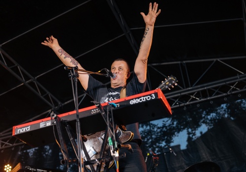 Tymon Tymański z uniesionymi rękami, stojący na scenie podczas koncertu wydarzenia „35. URODZINY FORMACJI TOTART”.