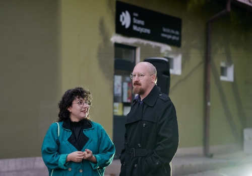 Kadr na Korę Kowalską oraz Szymona Szyszko na tle wejścia do sklepu muzycznego, podczas wydarzenia „PRZYSTAŃ. PAWEŁ BŁĘCKI”.