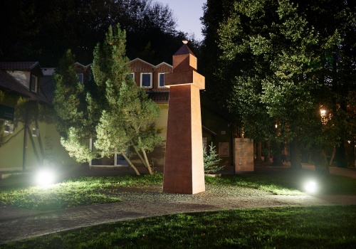 Fotografia przedstawiająca intensywnie oświetlony, schematycznie wykonany obiekt z drewna, przypominający latarnię morską, którego autorem jest Paweł Błęcki. Fotografia wykonana podczas wydarzenia „PRZYSTAŃ. PAWEŁ BŁĘCKI”.