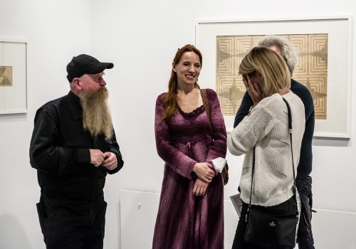 Zdjęcie rozmawiających ze sobą gości wystawy "935 ruchów w nieskończonej linii Wacława Szpakowskiego"oraz dzieła prezentowane na wystawie "w przestrzeni wystawienniczej CSW Łaźnia.