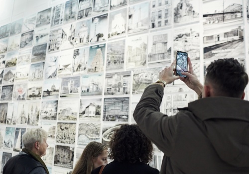 Zdjęcie. Grupa osób oglądająca wystawę. Jeden z mężczyzn fotografuje wystawę smartfonem. 
