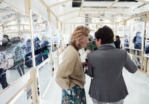 Zdjęcie. Dwie rozmawiające kobiety wewnątrz instalacji artystycznej „Arkadia”. Instalacja złożona z drewnianej konstrukcji, na której rozwieszone są grawerowane lustra.
