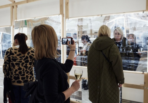 Zdjęcie. Grupa osób wewnątrz instalacji artystycznej „Arkadia”. Jedna z kobiet fotografuje smartfonem drugą kobietę na tle grawerowanych luster. 