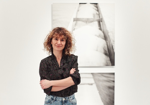 Zdjęcie. Portret artystki Anny Kędziory na tle fotografii wiszących na ścianie.