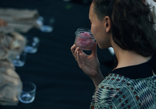 Zdjęcie. Kobieta widoczna z boku. Wącha potrawę w kolorze różowym, która znajduje się w słoiku.