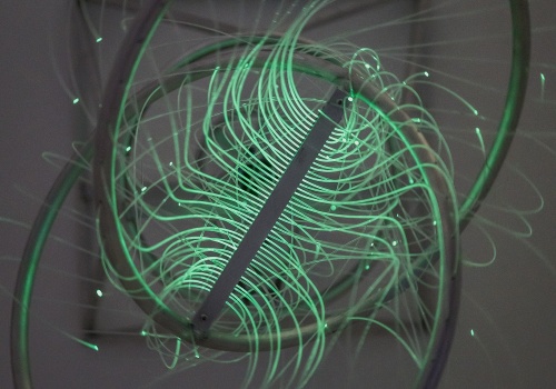 Zdjęcie. Praca Londona Tsai’a „Obrotowa kula Hopf'a: A Dream Machine” składająca się z dwóch metalowych obręczy i sieci zmieniających kolor światłowodów, na zdjęciu w kolorze zielonym.