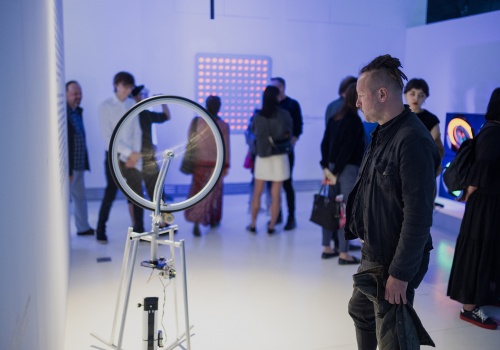  Zdjęcie. Przestrzeń wystawy. Mężczyzna przyglądający się pracy Londona Tsai’a „Duchamp Cybernetyczny”.