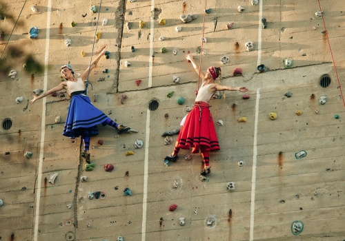 Zdjęcie. Dwie kobiety ubrane w kolorowe stroje inspirowane tradycją kaszubską wiszące na linach, na ściance wspinaczkowej.