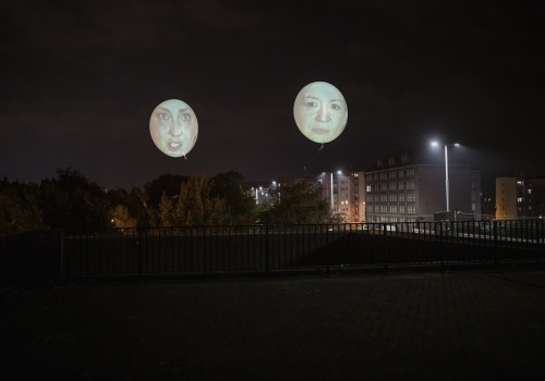 Widok na powietrzny performans - dwa ponad dwumetrowe balony na których wyświetlone zostały twarze kobiet, uczestniczek projektu. Widoczny również teren dachu Gdańskiego Teatru Szekspirowskiego. W tle widok na panoramę Gdańska.