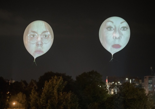 Zbliżenie na dwa ponad dwumetrowe balony na których wyświetlone zostały twarze dwóch kobiet, uczestniczek projektu. W tle widok na nocne niebo i na panoramę Gdańska.