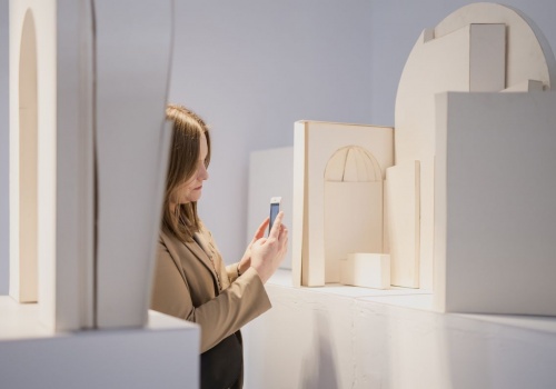 Kobieta ujęta z profilu, w trakcie fotografowania smartfonem, części modelu pawilonu polskiego na Biennale w Wenecji projektu prof. Jacka Dominiczaka.