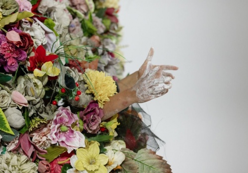 Zdjęcie. Z pracy artystycznej –trenu z kwiatów, wystają ubrudzone gipsem ręce performerki Dominiki Kimaty.